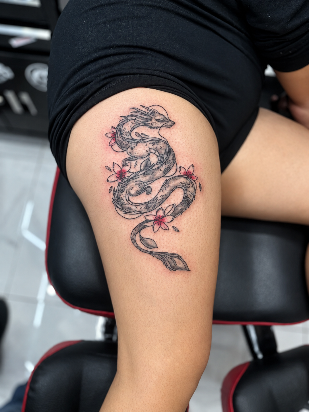 Tatouage fine line représentant un dragon et des fleurs rouges