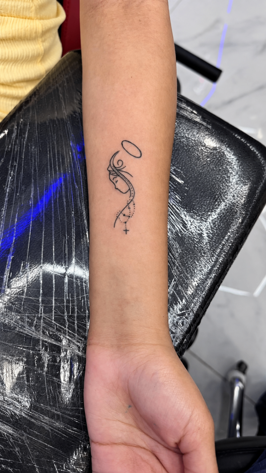 Tatouage Fine Line d’un profil avec halo et rosario sur l’avant-bras