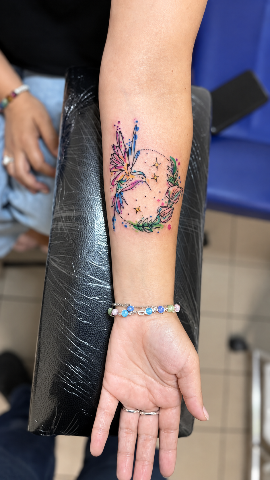 Tatouage New School d’un colibri entouré de fleurs colorées
